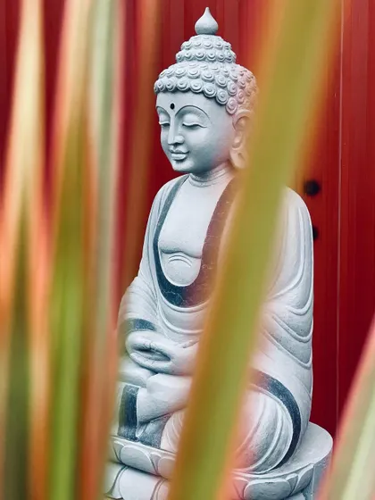 An artistic shot of a stone Buddha statue, viewed through colorful foliage.