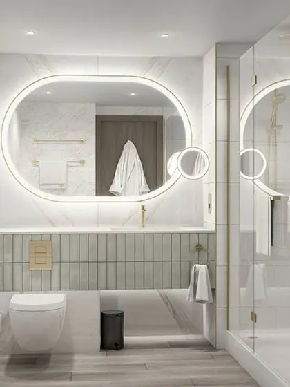A bright and modern bathroom in all-white and light grey tones. The large, oblong back-lit mirror and glass shower create a clean and spacious feel.
