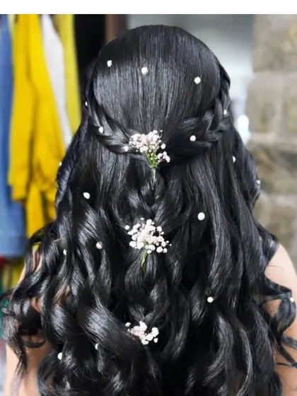 A romantic half-up style with a waterfall braid, curls, and scattered pearl and flower accents.