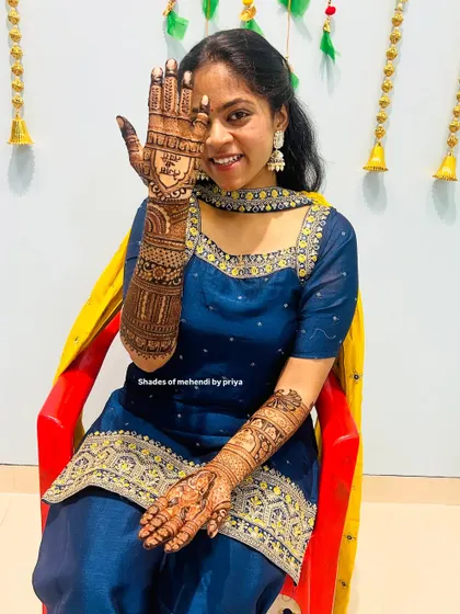 A happy bride showing off her detailed mehendi. The design includes a portrait on the palm and extends all the way up her arm.