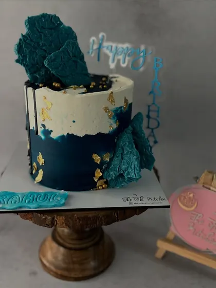 This abstract design uses shades of deep blue and white buttercream, accented with gold leaf and topped with dark blue chocolate sails.