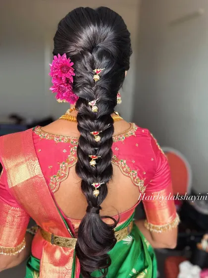 A close-up of the bridal hairstyle, a thick, neat braid decorated with a fresh flower and traditional hair accessories. This style pairs beautifully with South Indian bridal sarees.