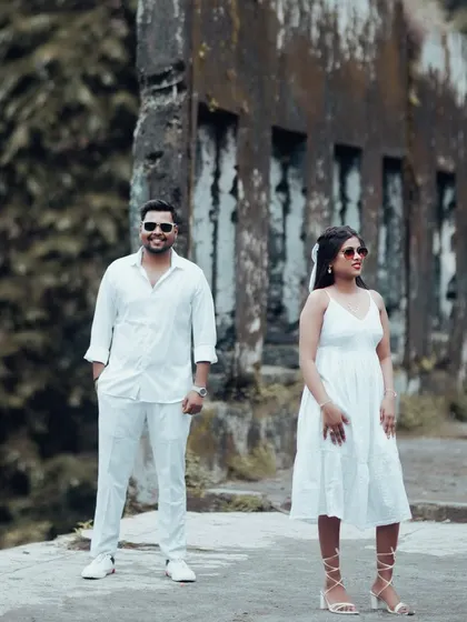 A cool and confident pose from a couple in all-white attire, standing against a textured, aged wall for a modern pre-wedding portrait.