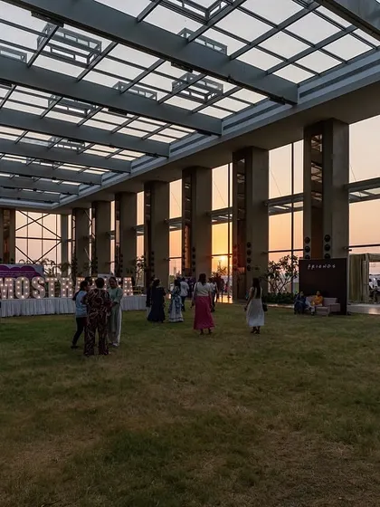 As dusk settles, the pavilion transforms into a glowing beacon. The structure's transparency creates a beautiful effect, with the interior activities visible from the outside and the sunset providing a stunning natural backdrop.