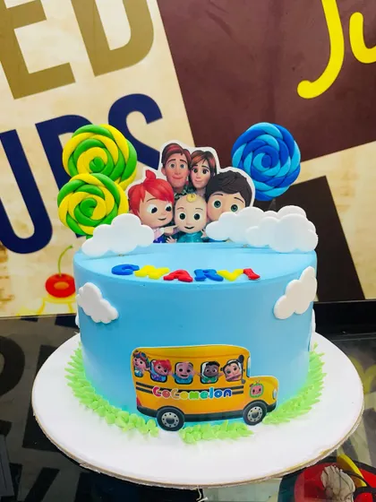 A 1.5kg Cocomelon cake featuring the iconic yellow school bus and colorful lollipop toppers.