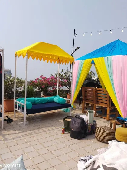 A daytime view of a terrace decoration in Bandra, featuring colorful cabanas and swing seating for a relaxed and festive event.