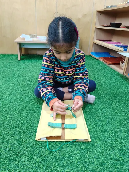 A child practices tying bows on a dressing frame. This activity directly helps a child learn to tie their own shoelaces, fostering independence in self-care.