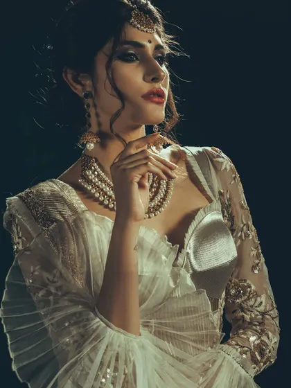 A close-up shot highlighting the texture of the modern white saree and the layered pearl necklace. The lighting carves out the details, creating a sophisticated and high-contrast image.