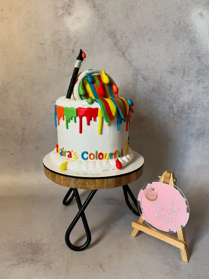 A cake for a budding artist, designed to look like a bucket of paint spilling rainbow colors down the side. The paintbrush and other details are all edible creations.