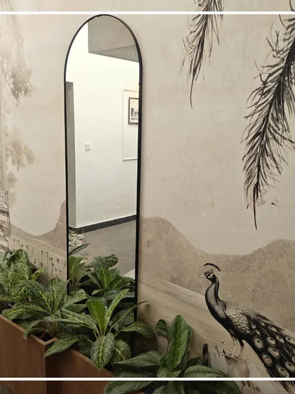 An arched mirror elongates the passage and reflects the heritage-themed wallpaper, creating an illusion of greater space and light. The addition of indoor plants in a wooden planter introduces a biophilic element, softening the architecture.