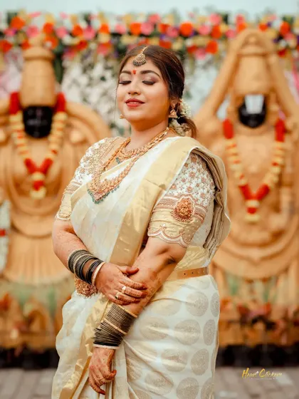 A serene portrait of the bride in her beautiful white and gold saree, standing in front of the wedding deities.