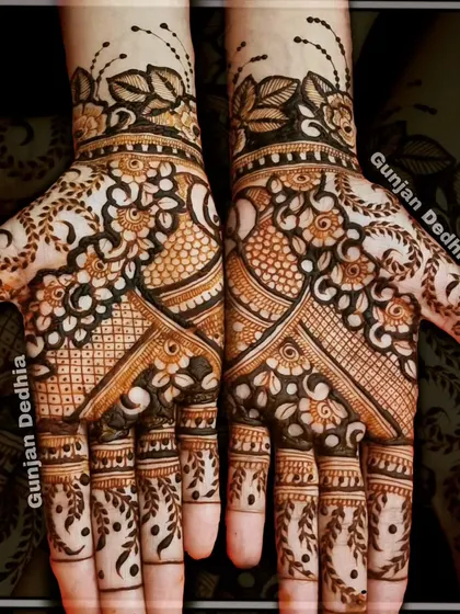 A full-coverage Indian mehendi design. The pattern combines floral elements, peacock motifs, and leafy vines on the fingers for a dense and beautiful look.