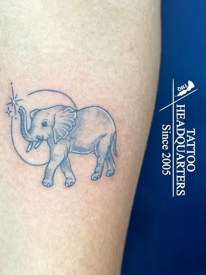 A fine-line elephant tattoo within a crescent moon, with a sparkling star, a whimsical and gentle design.