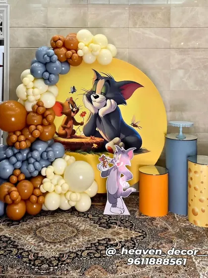 A nostalgic Tom and Jerry themed setup with a unique color palette of dusty blue, brown, and cream balloons. The decor features a large circular backdrop with the classic characters, themed plinths including one designed like cheese, and a character cutout.