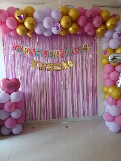 A simple birthday party backdrop for a home celebration, featuring a purple shimmer curtain and a balloon arch in pink, purple, and gold.