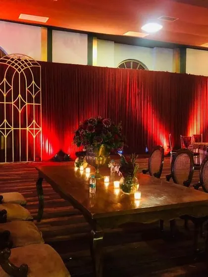 The guest dining area for the royal red wedding theme. I used long wooden tables with vintage-style chairs and simple candle centerpieces, all set against a backdrop of red velvet drapes and warm uplighting to maintain the regal ambiance.