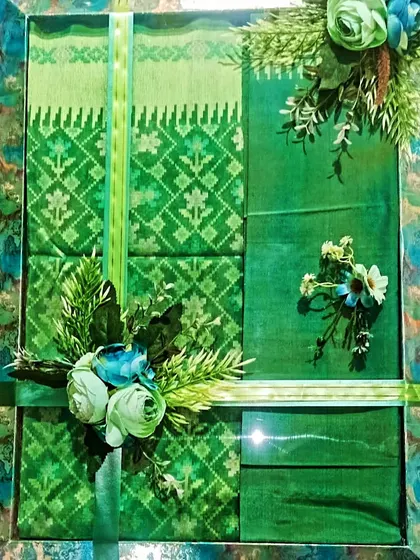 A green saree packed in a matching green patterned box with floral decorations.