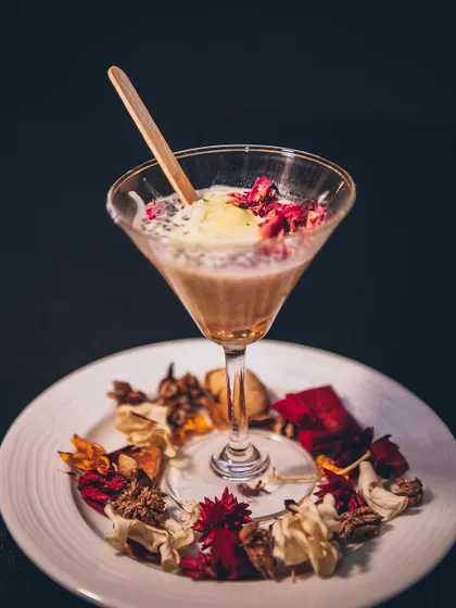 A beautifully plated dessert in a martini glass, garnished with dried flowers and rose petals.