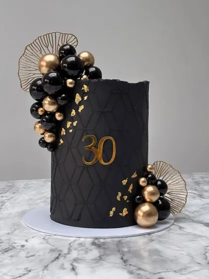 A sophisticated black and gold cake for a 30th birthday. This design features a geometric pattern, gold leaf, and dramatic black and gold balloon-like spheres.