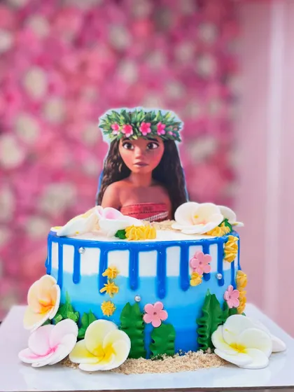 An adventurous 'Moana' themed cake. The design captures the spirit of the movie with tropical flowers, ocean waves, and a Moana character topper.