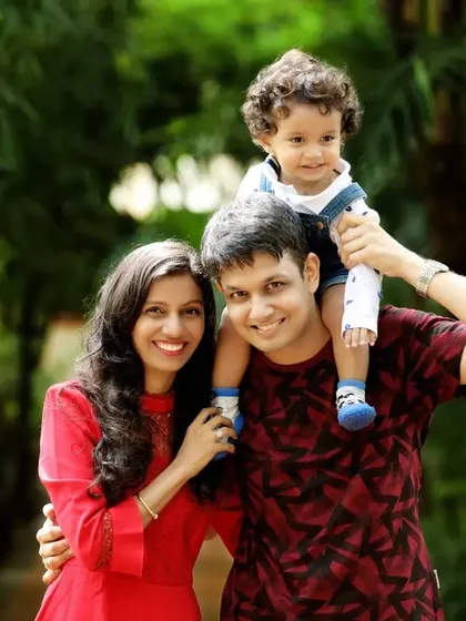 A classic family pose with the little one enjoying a ride on dad's shoulders. The lush green background of the park adds a vibrant, natural feel to this happy family portrait.