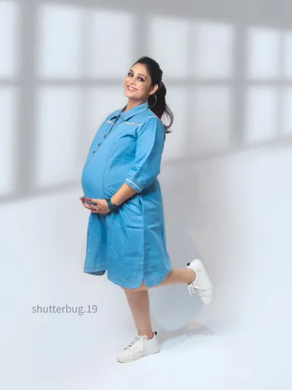 A cheerful and casual solo portrait of the mom-to-be in a cute denim dress. This shot complements the "Vogue cover" concept, showing a more relaxed but equally stylish side.