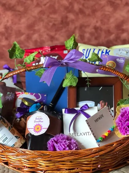A beautifully arranged Rakhi basket decorated with artificial vines and flowers. It contains a photo frame, snacks, and beauty products.