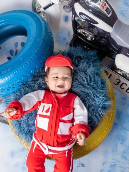 A few action shots from an F1 and racing-inspired photoshoot. The baby is styled in a red racing uniform, captured with fun expressions among tires and toy vehicles.