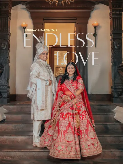A regal portrait of Abhinav and Paromita, titled 'Endless Love.' Their traditional red and white outfits stand out against the classic architectural backdrop.