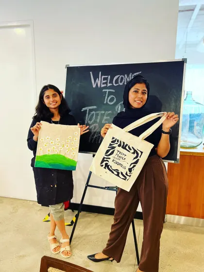 Two participants showing off their finished hand-painted tote bags. Each one is a unique expression of their personal style.