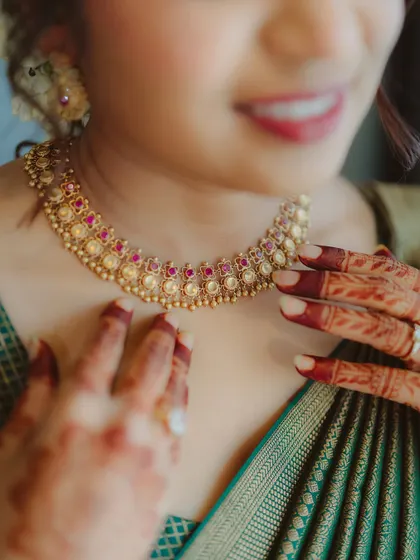 A close-up of a bride's traditional gold and ruby necklace and her henna-stained hands. This image focuses on the rich colors and textures of her South Indian bridal look.