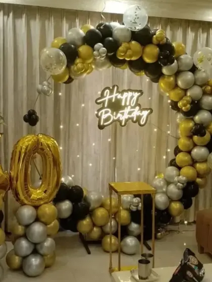 A sophisticated 40th birthday decoration in black, gold, and silver. This setup includes a circular balloon arch, a "Happy Birthday" neon sign, and large foil number balloons.