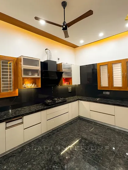 A spacious U-shaped kitchen featuring white cabinets, a black granite countertop, and a black chimney. The wooden-framed windows and upper cabinets add a touch of traditional warmth to the modern design.