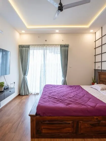 A cozy bedroom with warm wood tones, soft ceiling lighting, and a stylish accent wall. The floating TV unit maintains the clean, modern aesthetic.