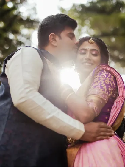 A sun-kissed, romantic portrait. The beautiful backlighting and the groom's affectionate kiss create a warm, dreamy, and intimate image.