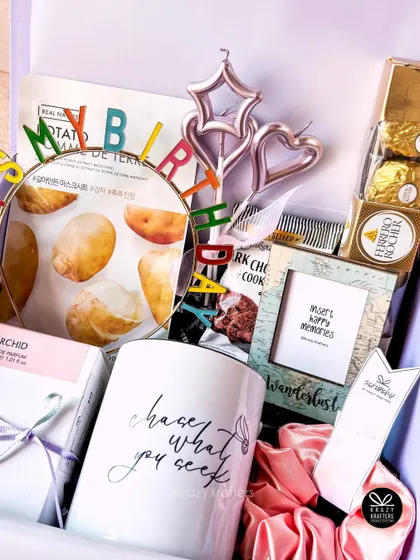 A fun and girly birthday hamper with a 'chase what you seek' mug, a 'Happy Birthday' headband, face masks, and Ferrero Rocher chocolates.