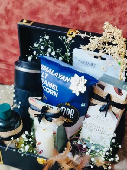 A sophisticated Rakhi hamper for him in a black trunk box. It includes a sipper, gourmet popcorn, cookies, and a face mask.