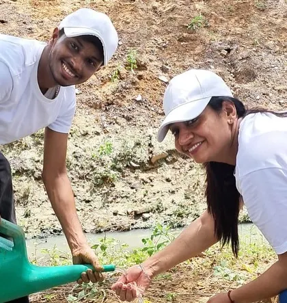 Two smiling volunteers from Orbis Financial water a newly planted sapling, helping to enhance the soil health of the creek's banks.