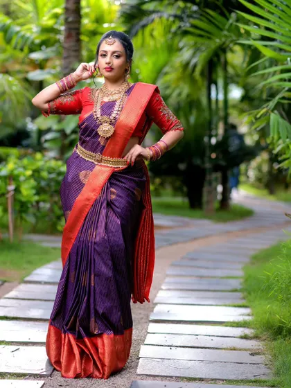 Another angle of the purple and red silk saree, showing its beautiful drape and the traditional gold jewelry that completes the look.