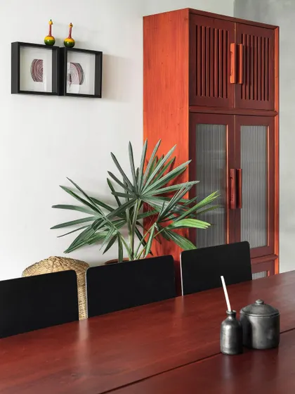 A detail shot of the dining area in 'Rustic Minimal', showcasing the rich color of the mahogany furniture against a neutral wall. Small, curated decor pieces add a personal touch.