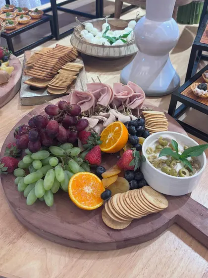 A classic charcuterie board featuring rolled cured meats, a variety of crackers, fresh grapes, berries, and a basil-topped dip. This platter offers a balanced selection of savory and sweet flavors.