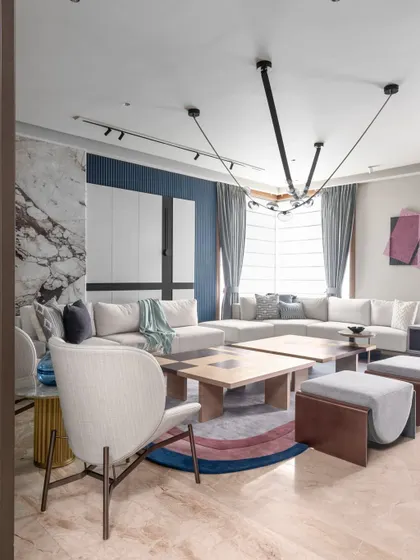 A view of the living area showcasing the interplay of textures and light. The design combines a plush sectional sofa, a unique split coffee table, and a sculptural light fixture to create a dynamic yet harmonious environment.