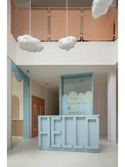 A full view of the reception area, with its friendly "HELLO" desk, cloud-shaped pendant lights, and soft pastel color palette. It sets a whimsical and welcoming tone for the entire nursery school.