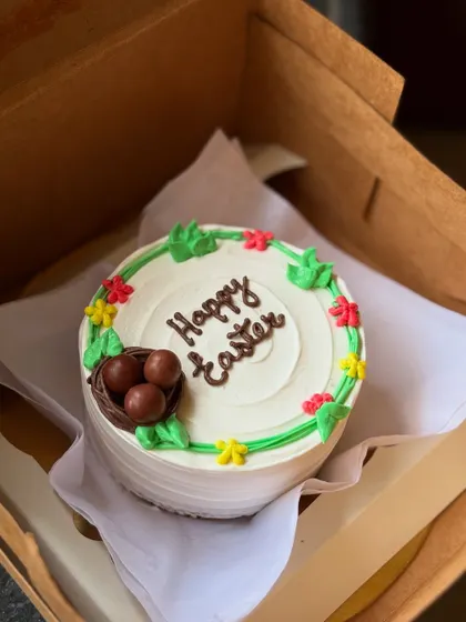 A festive "Happy Easter" bento cake. This design features a cute little bird's nest with chocolate eggs, surrounded by colorful flowers, perfect for an Easter celebration.
