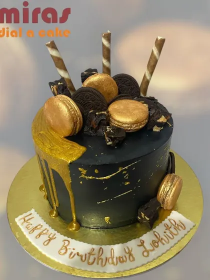 A sophisticated black and gold chocolate cake. The dark cake is adorned with a shimmering gold drip, golden macarons, and Oreos, making it a stylish and decadent birthday choice.