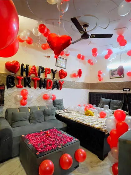 The living room is transformed for a birthday celebration with balloons on the ceiling and a coffee table covered in rose petals.
