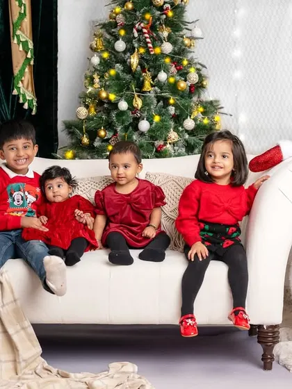 A group of adorable children sitting together on the couch, all dressed in red for their Christmas photoshoot.