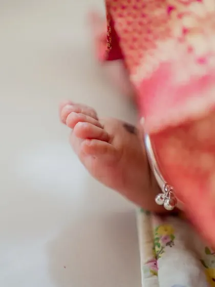 The tiniest feet make the biggest footprints in our hearts. A close-up of the baby's foot and silver anklet, a classic detail from a newborn photoshoot or naming ceremony.