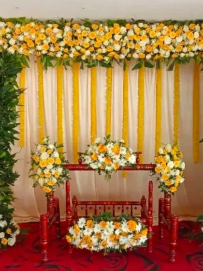A traditional decor setup for an engagement or naming ceremony, featuring a yellow and white floral backdrop with a decorated wooden cradle.