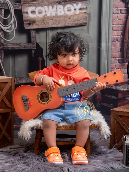 This little musician is ready to play a tune in our cowboy themed studio. The rustic backdrop and props like the small guitar add a playful, storybook feel to the portrait.